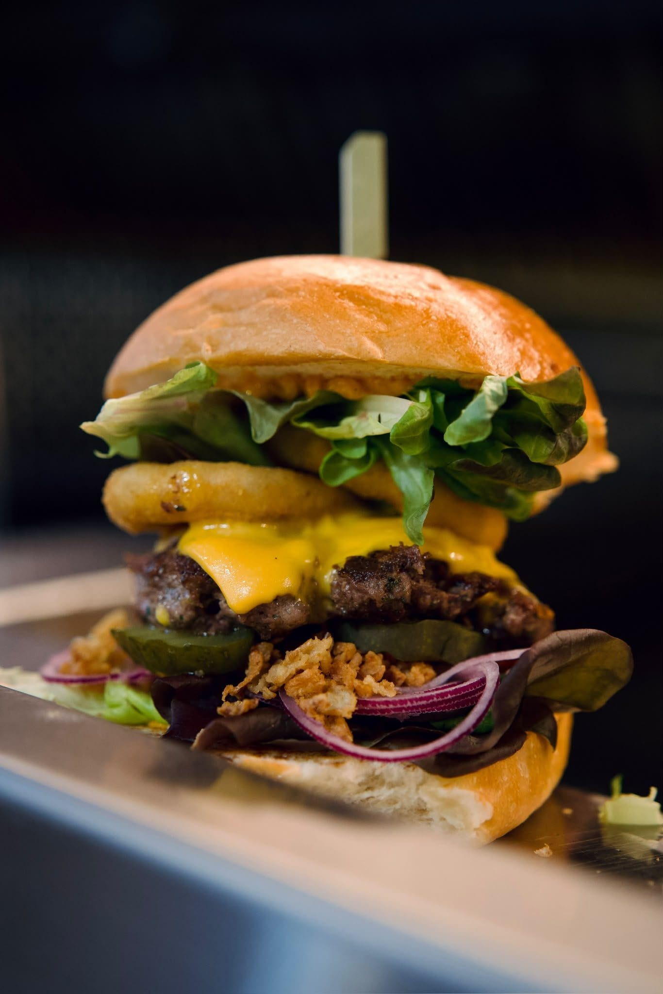Un burger au cheddar et aux oignons frits, posé sur le plan de travail en inox.
