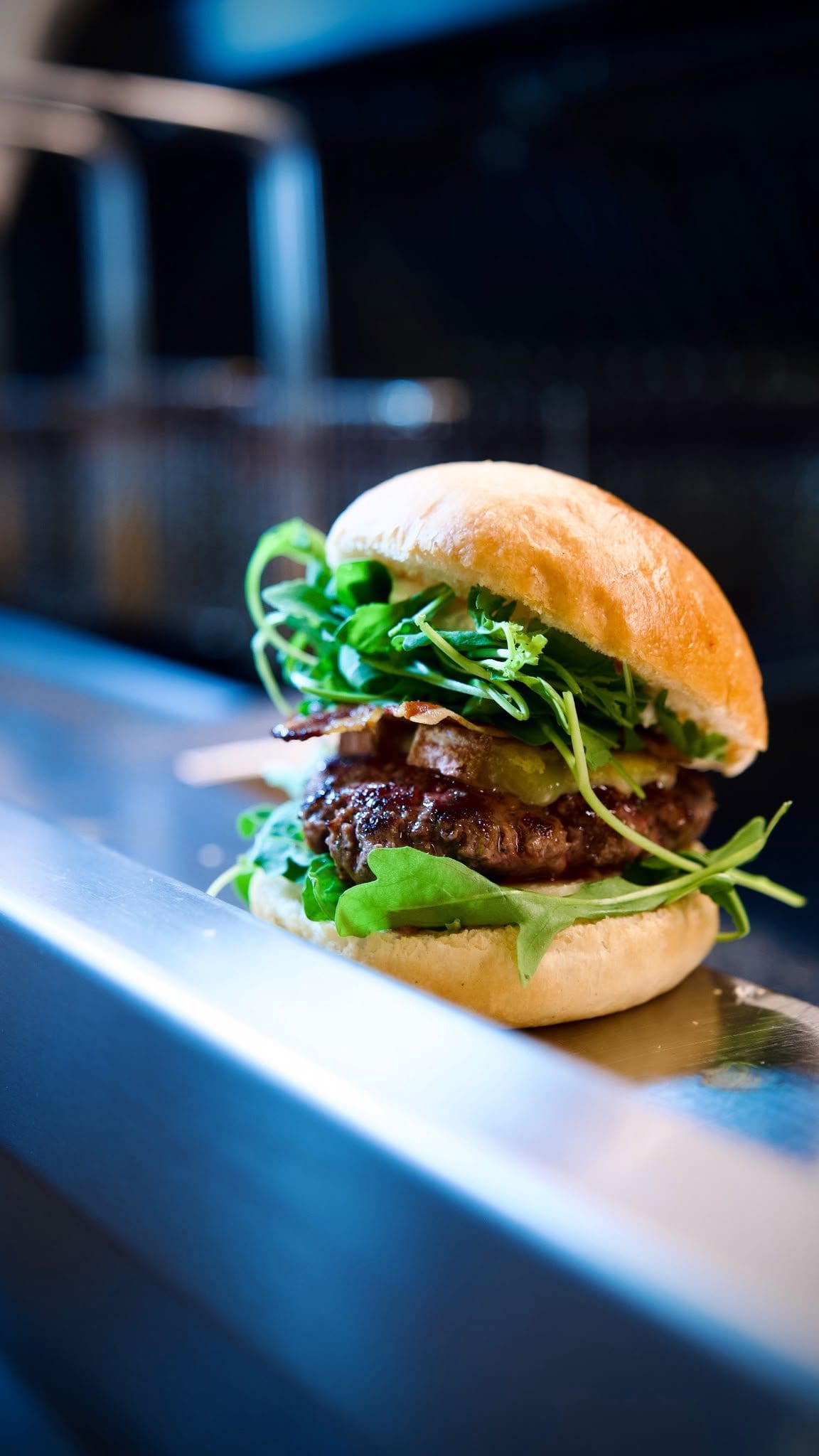 Un burger garni de roquette, posé sur le comptoir en inox.