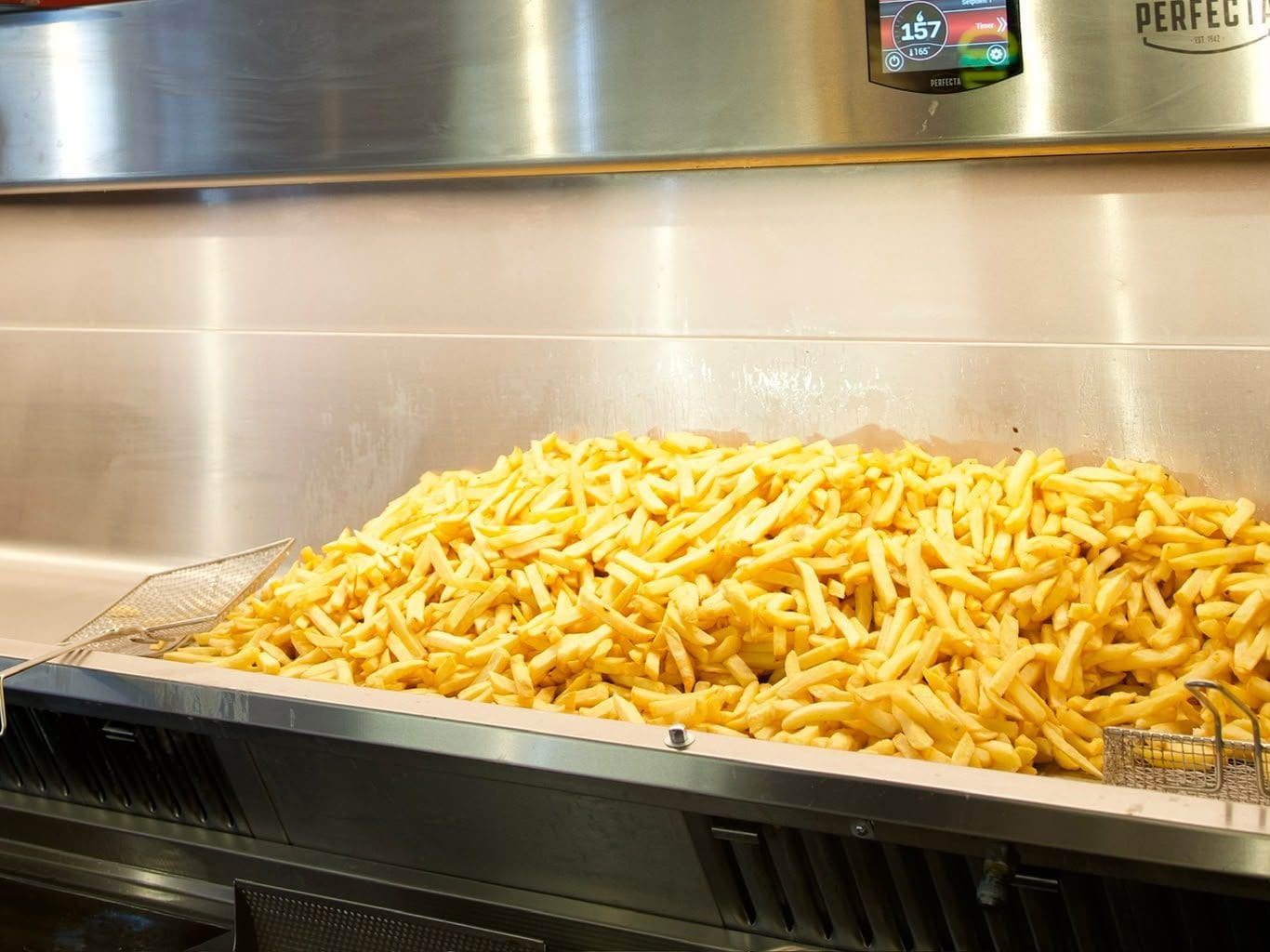 Un bac de frites fraîches sur le plan de travail en inox, paniers de friteuse posés à côté.