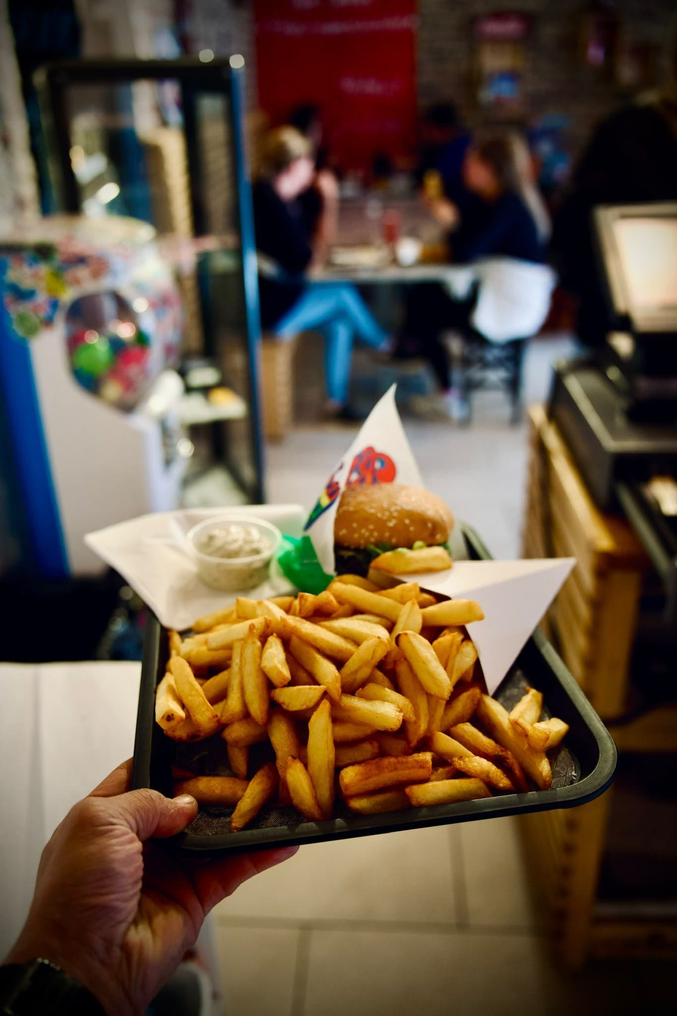 Une barquette de frites tenue à la main devant la salle de la friterie.